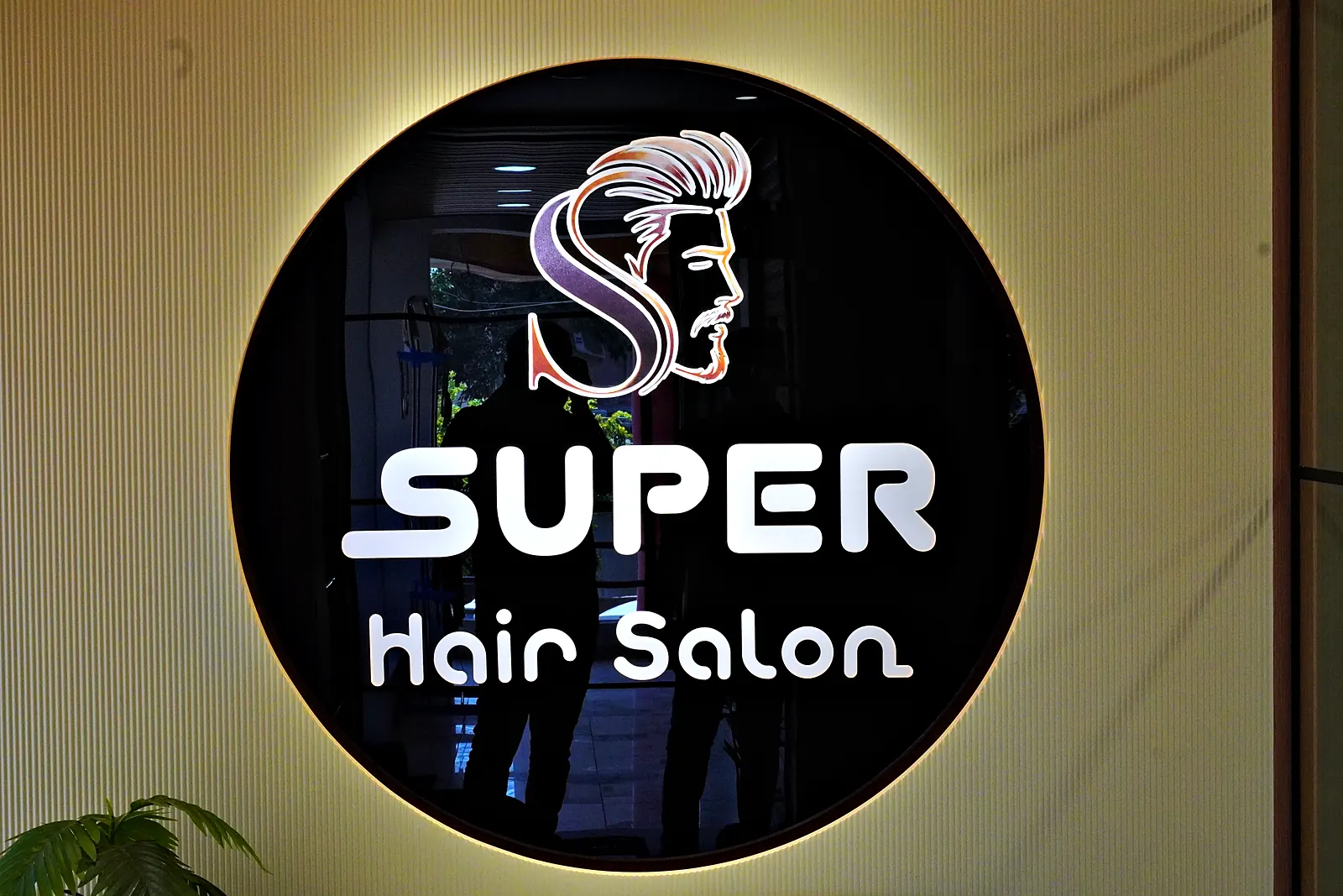 Backlit round SUPER Hair Salon logo on the wall
